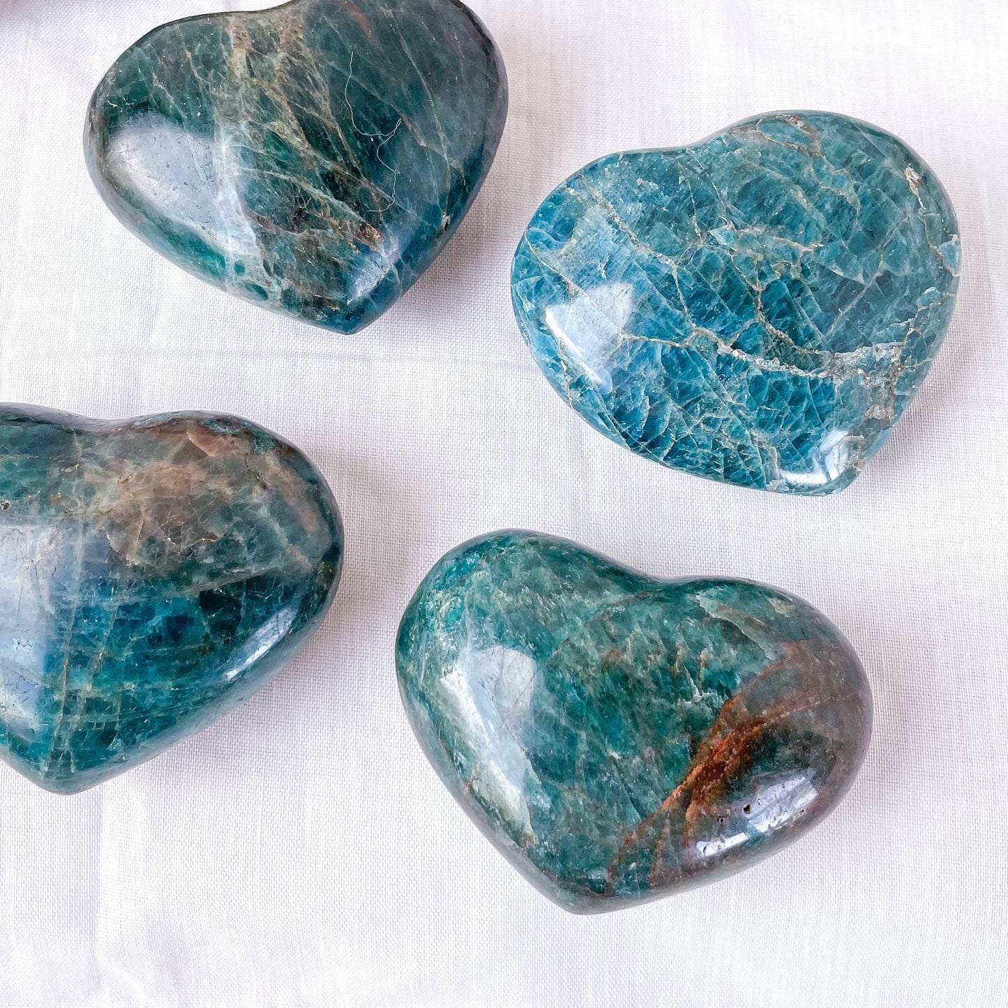 Four heart-shaped blue stones on a white background. A greenish-blue apatite crystal stone in shape of heart.