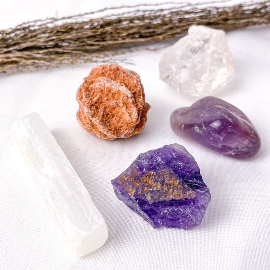 Mineral samples including a white crystal, brown crystal, purple crystal, and a white rod on a white background.