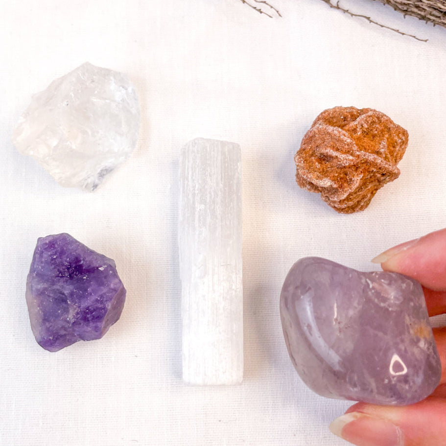 Collection of crystals including amethyst, rose quartz, and selenite on a white surface.