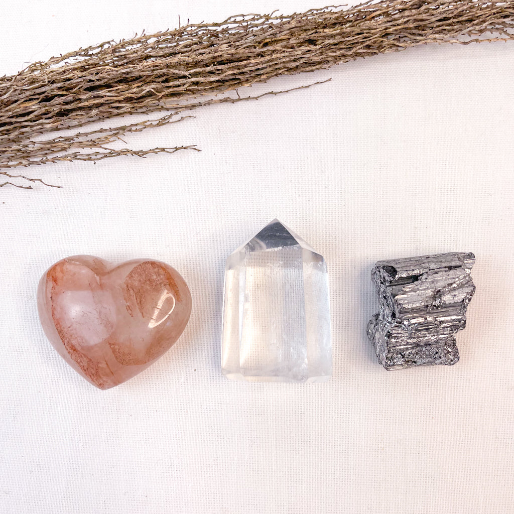 Heart-shaped stone, crystal, and pyrite on a white surface with twigs.