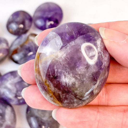 Hand holding a purple amethyst crystal with more crystals in the background