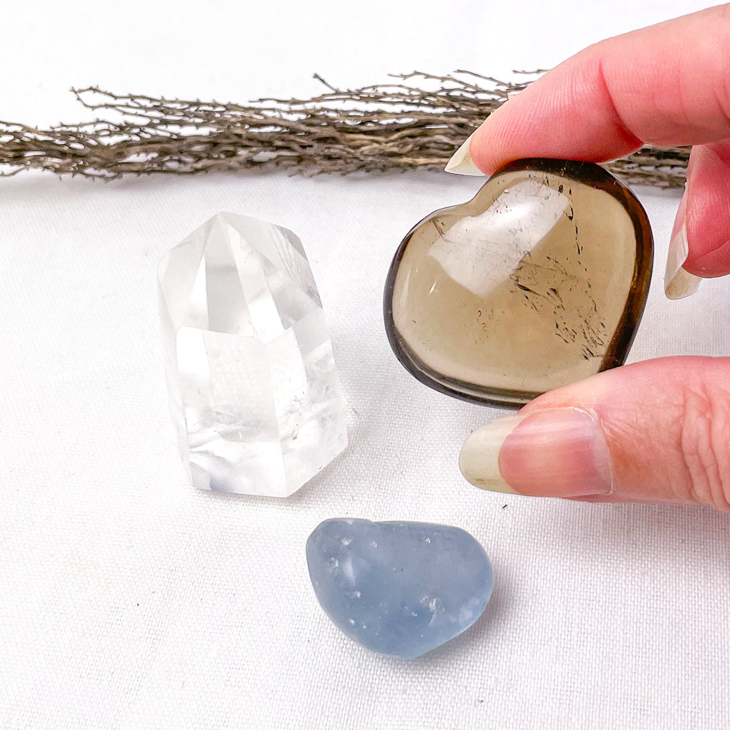 Heart-shaped crystal held by a hand with clear and blue crystals on a white background