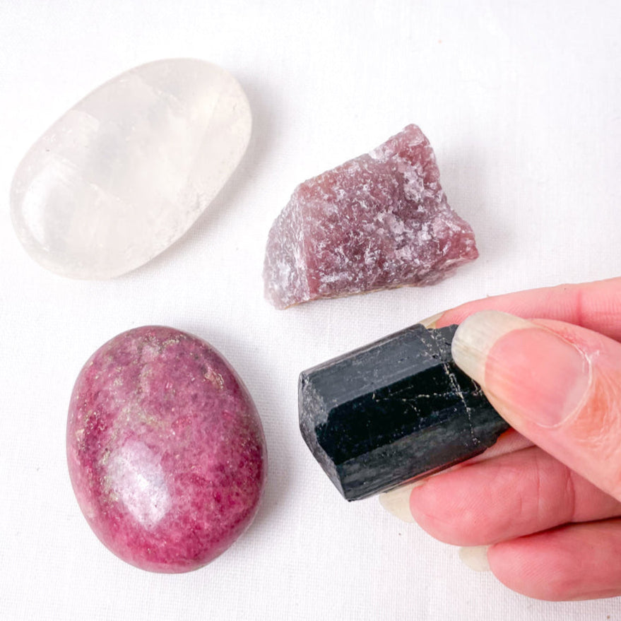Hand holding a black crystal next to two pink crystals on a white surface