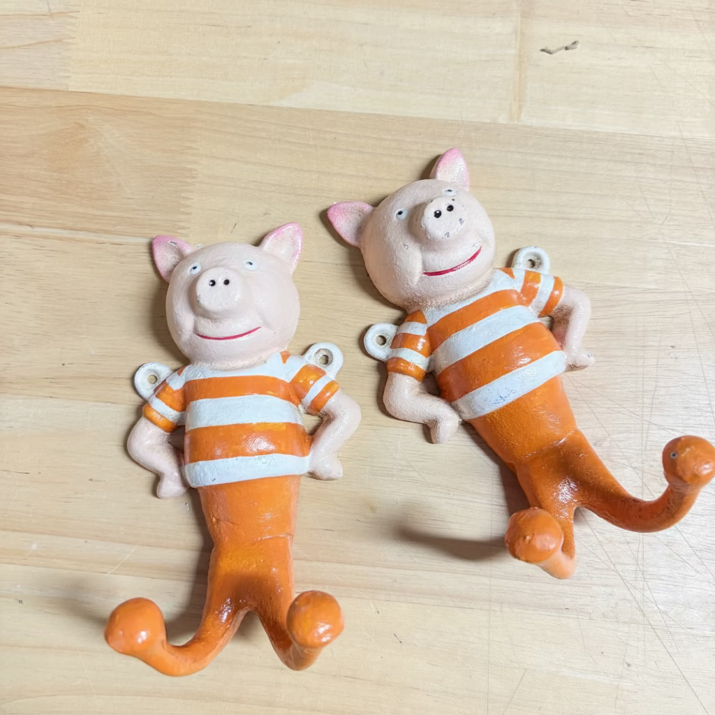 Two pig hooks wearing orange-and-white striped shirts, placed on a light wood surface.