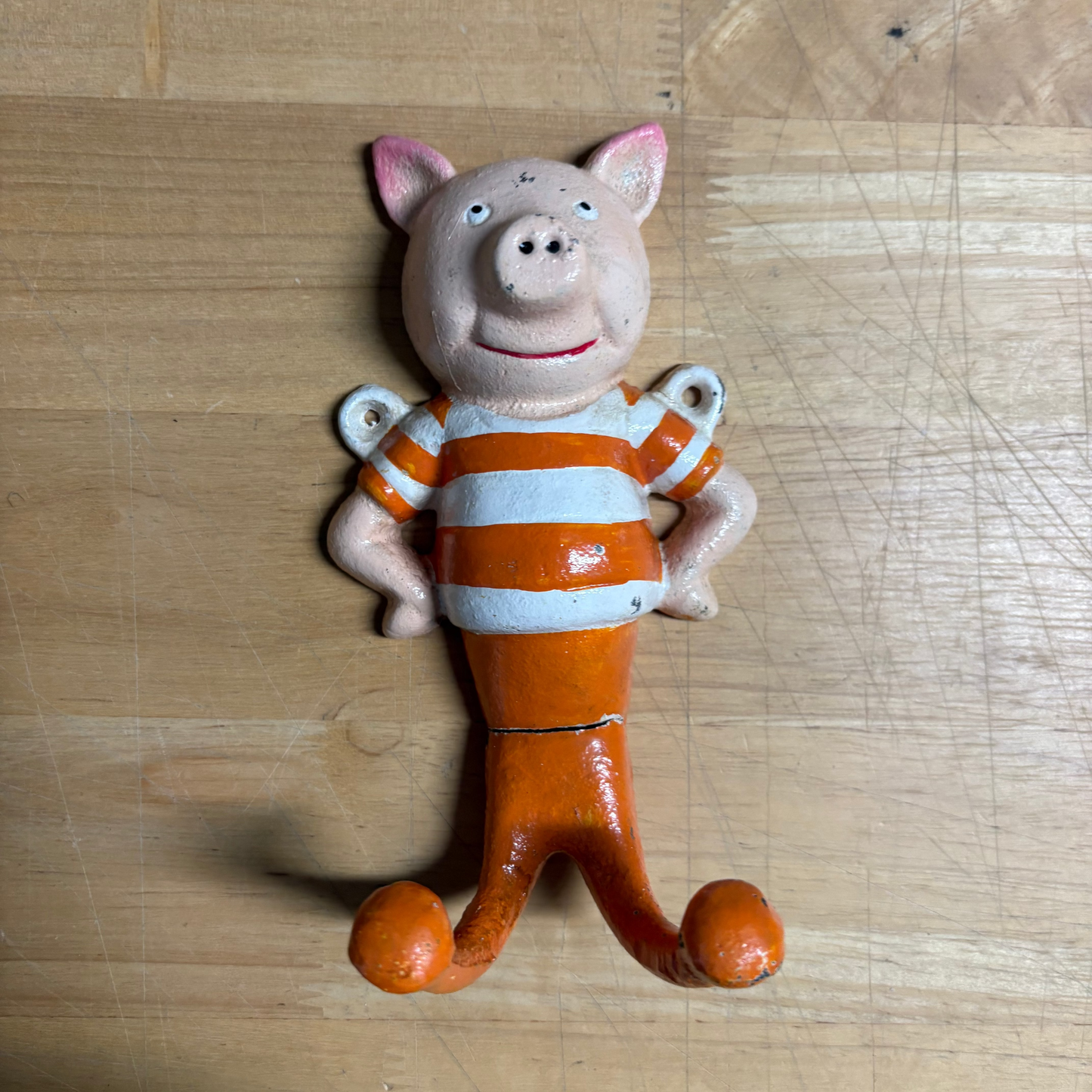 A small pig shaped hook wearing an orange and white striped shirt, standing on a light wood surface.