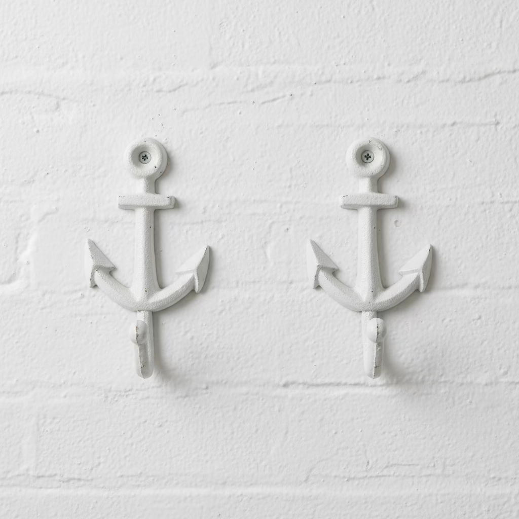 A pair of white-painted cast iron anchor wall hooks displayed on a scratched wooden tabletop.