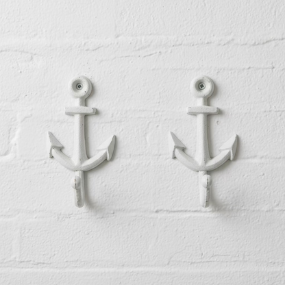 A pair of white-painted cast iron anchor wall hooks displayed on a scratched wooden tabletop.