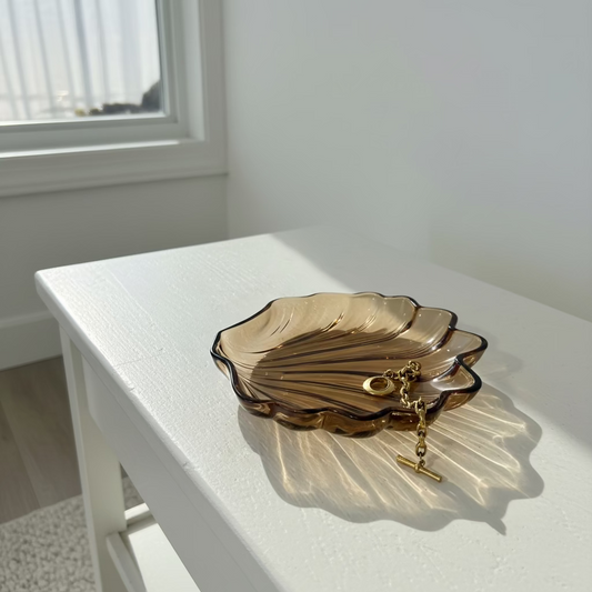 A scallop-shaped glass dish with a gold chain, set against a plain white background.