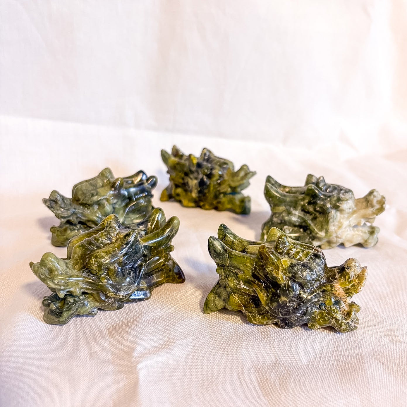 Five greenish-brown decorative crystal dragon head stones on a white surface