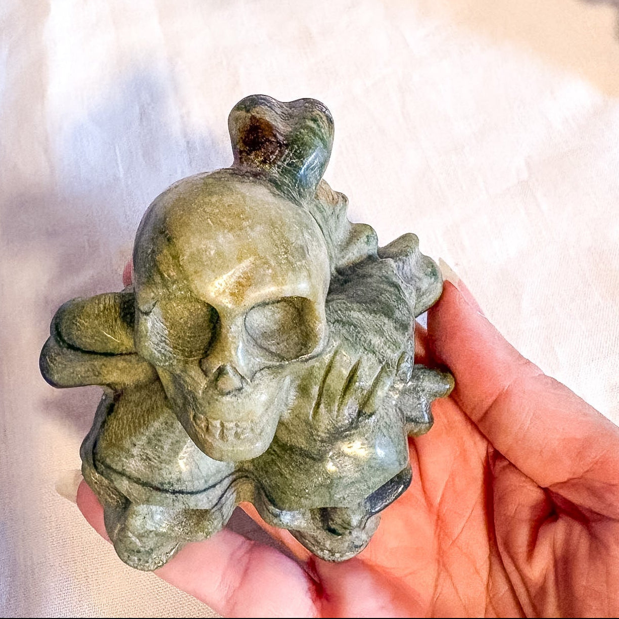 Green stone skull figurine held in a hand against a white background