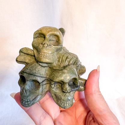 Hand holding a green stone skull sculpture against a white background