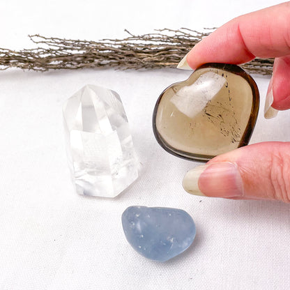 Heart-shaped crystal held by a hand with clear and blue crystals on a white background