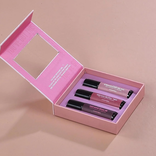 Pink box containing three roll-on bottles with product details on a beige background