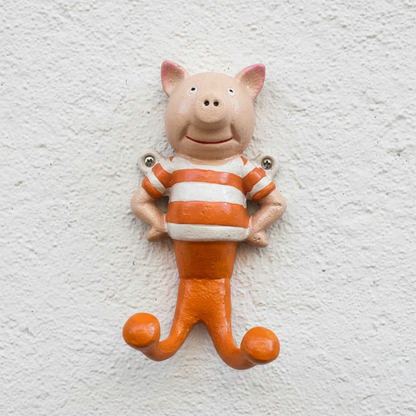 A pig-shaped decorative wall hook with a pinkish-beige head, orange and white striped shirt, and orange legs, shown against a plain white background.